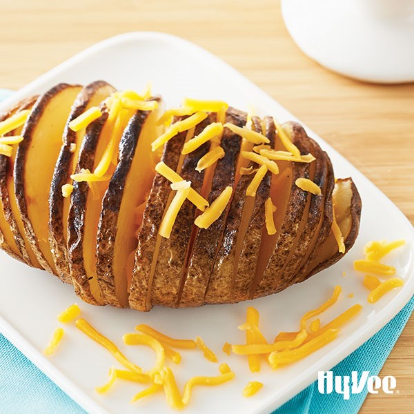 Skin-on hasselback potato garnished with shredded cheddar cheese on white plate