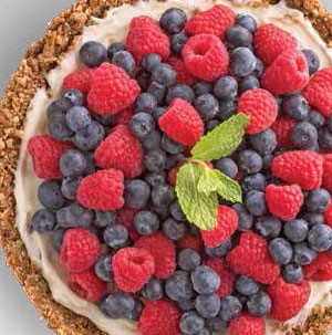 Tort topped with creamy filling, fresh blueberries and raspberries, and a fresh mint leaf for garnish