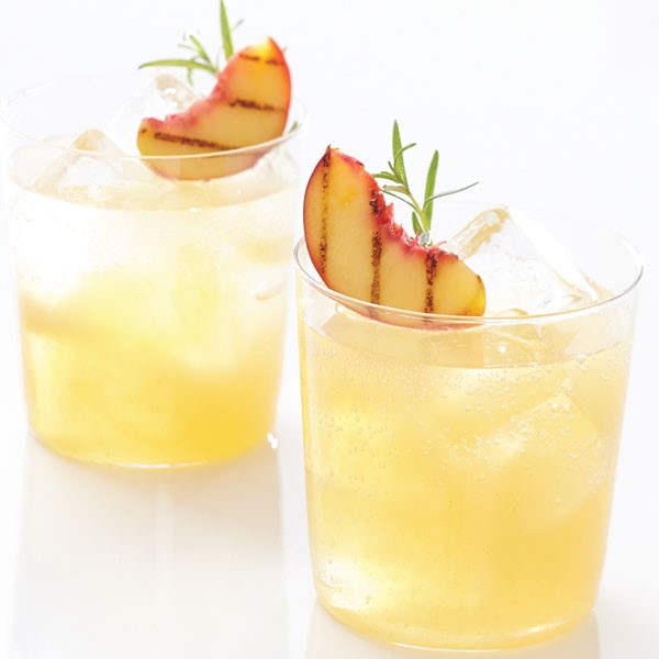 Two glasses of iced spritzer, garnished with grilled peaches and sprigs of rosemary