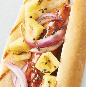 A hoagie filled with a teriyaki-barbecue marinated hot dog, pineapple chunks, red onion and black sesame seeds