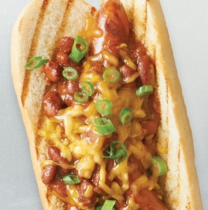 Hot dog and toasted bun topped with chili beans, cheddar cheese and green onions