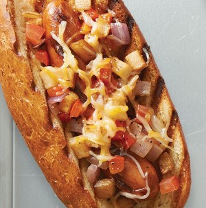 Hot dog and bun covered with hash browns, vegetables and cheese