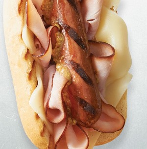 Grilled hot dog bun filled with cheese, sliced deli ham, grilled hot dog, and whole grain mustard