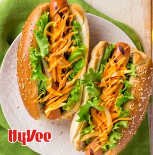 Two grilled hot dogs topped with spicy mayo, onion and carrots and placed in sesame seed hoagies