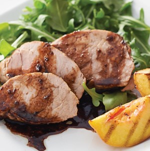 Sliced pork tenderloin glazed with balsamic vinegar aside grilled peaches and mixed greens