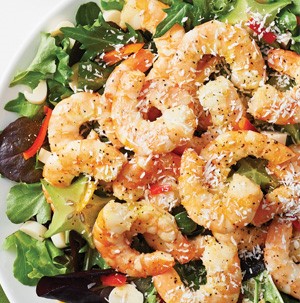 Bowl of salad topped with shrimp and coconut-pineapple vinaigrette and garnished with coconut flakes