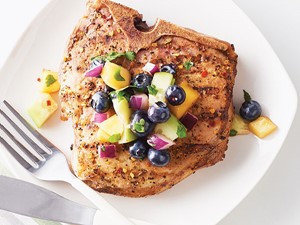 Seasoned pork chop topped with fruit salsa on a white plate with a fork and knife