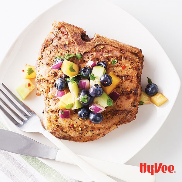 Seasoned pork chop topped with fruit salsa on a white plate with a fork and knife