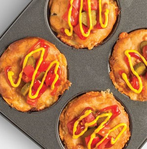 Cheeseburger pies in muffin tin with diced vegetables and drizzled with yellow mustard and ketchup