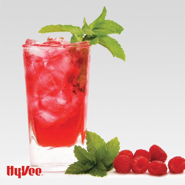 Raspberry jazz in a glass filled with ice cubes and garnished with mint leaves with additional fresh mint and raspberries on the side