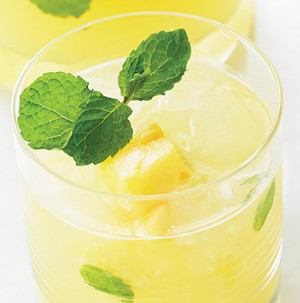 Glass of lemonade garnished with pineapple chunks and fresh mint