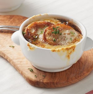 White bowl of french onion soup on a wooden plank
