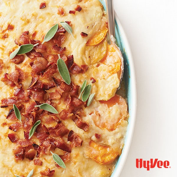 Bowl of potatoes au gratin, topped with bacon bits and fresh sage leaves