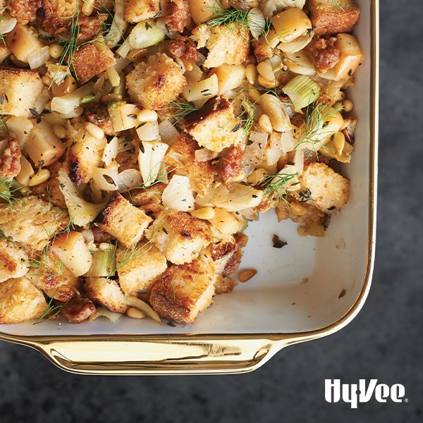 Casserole dish of sausage, fennel apple stuffing garnished with nuts and fennel fronds