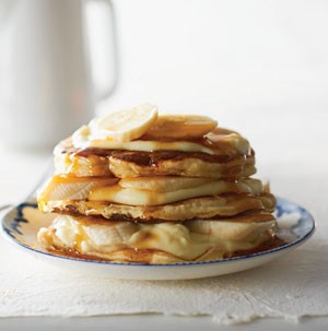 Stack of banana cream pancakes topped with syrup and fresh bananas on a blue-and-white plate