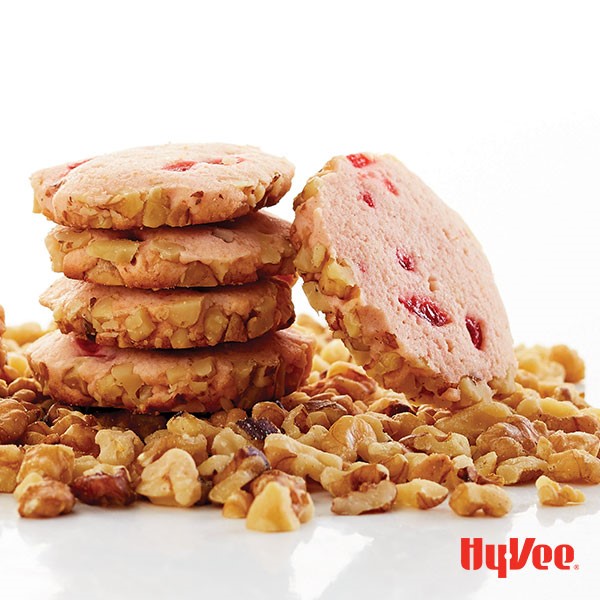 Stack of cherry icebox cookies over a layer of chopped walnuts