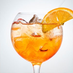 Wine glass filled with ice and orange beverage with orange wedge on rim