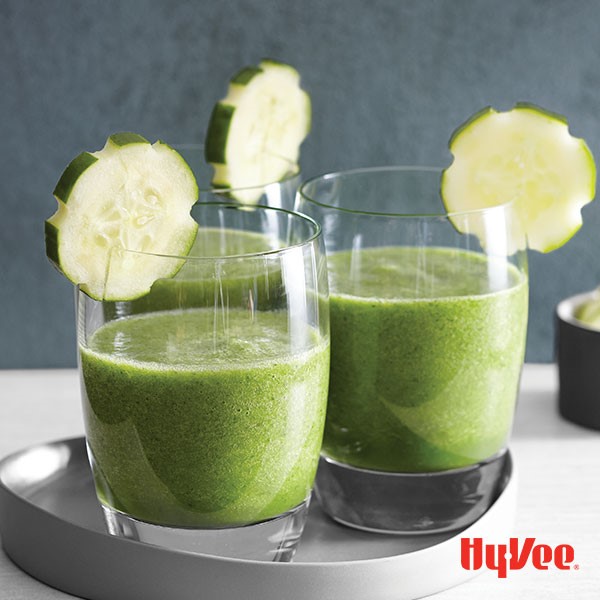 Kale smoothies in small glasses with a garnish of a cucumber slice on rim
