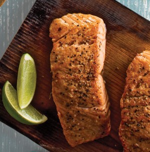 Seasoned salmon fillet on a wooden cutting board with lime wedges on side
