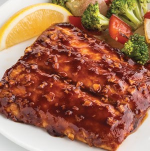Plate of barbecue-glazed salmon served with vegetables and lemon wedge