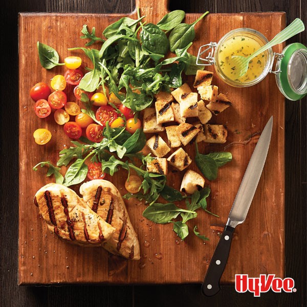 Wooden board of chicken panzanella served with side of dressing