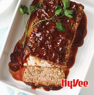 Glazed and sliced meat loaf on a white plate with a garnish of fresh parsley