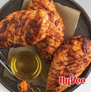 Seasoned grilled chicken breasts on plate with orange zest and olive oil