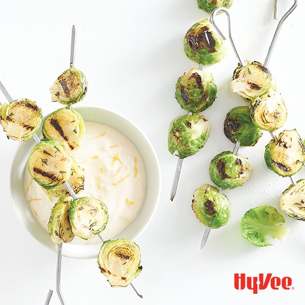 Grilled skewered brussels sprout halves over a bowl of lemon aioli