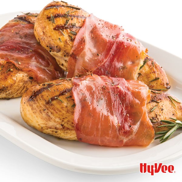 White plate with three prosciutto-wrapped chicken breasts, garnished with rosemary sprigs