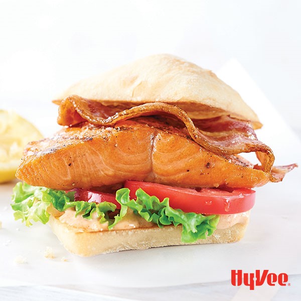 Bun topped with lettuce, sliced red tomatoes, grilled salmon fillet and cooked bacon strip