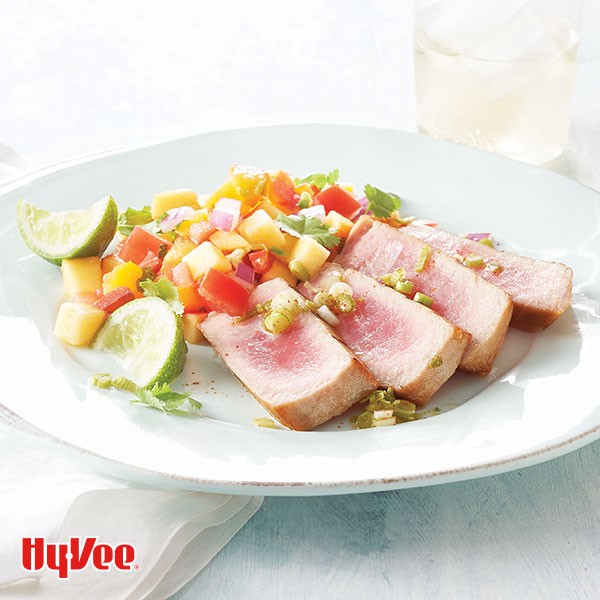 Grilled sliced tuna steaks with peach, red pepper, and red onion sauce garnished with fresh lime wedges