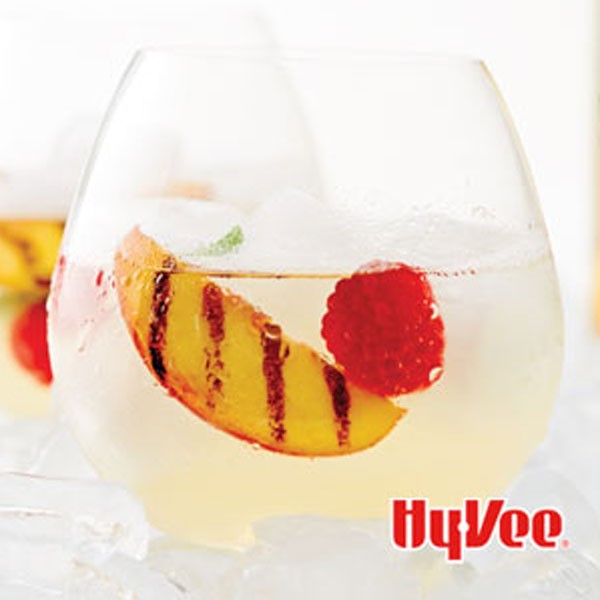 Glass of white sangria garnished with grilled peach slice and a raspberry