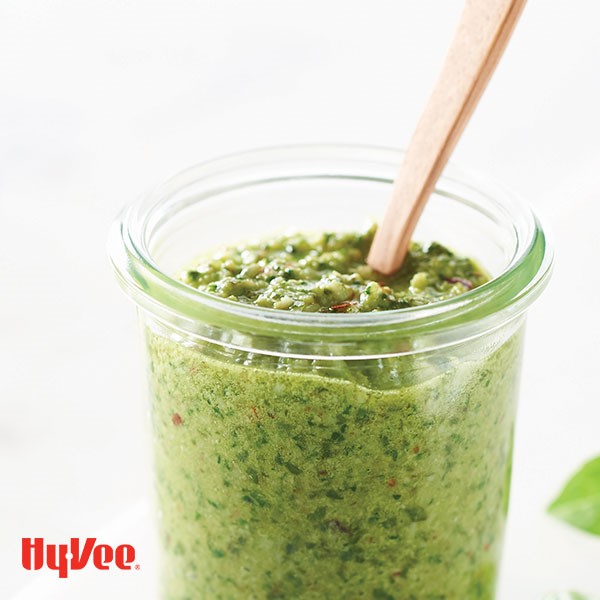 Glass filled with basil-spinach pesto and walnuts with a wooden spoon