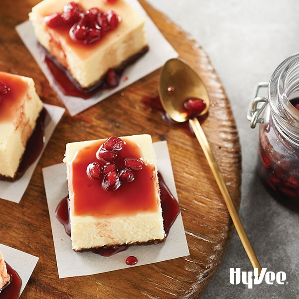 Cheesecake squares topped wth pomegranate sauce and seeds on parchment paper