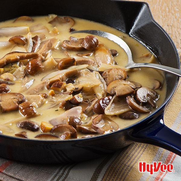 Sliced mushrooms, onions, and gravy in skillet with spoon