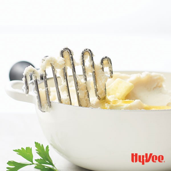 Bowl of mashed potatoes with butter and potato masher