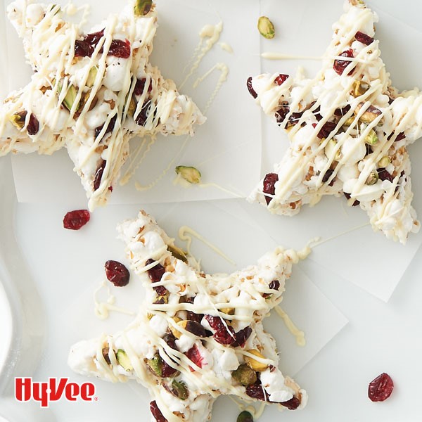 Cranberry-pistachio stars drizzled in melted white chocolate on parchment paper