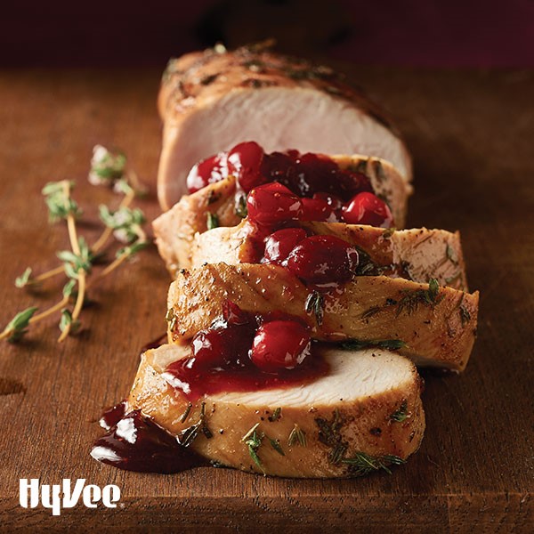 Thyme-rubbed sliced turkey tenderloins with whole cranberry sauce on wooden cutting board