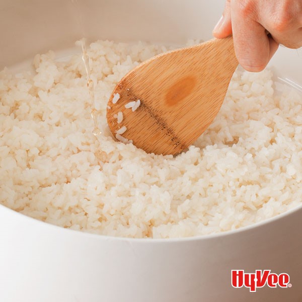 Bowl of sticky sushi rice with a person holding a wooden spoon