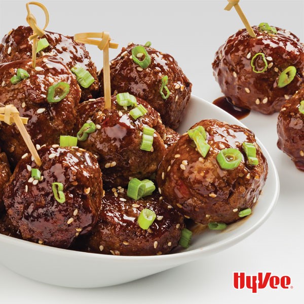 Meatballs glazed with teriyaki sauce and garnished with sesame seeds and sliced green onions