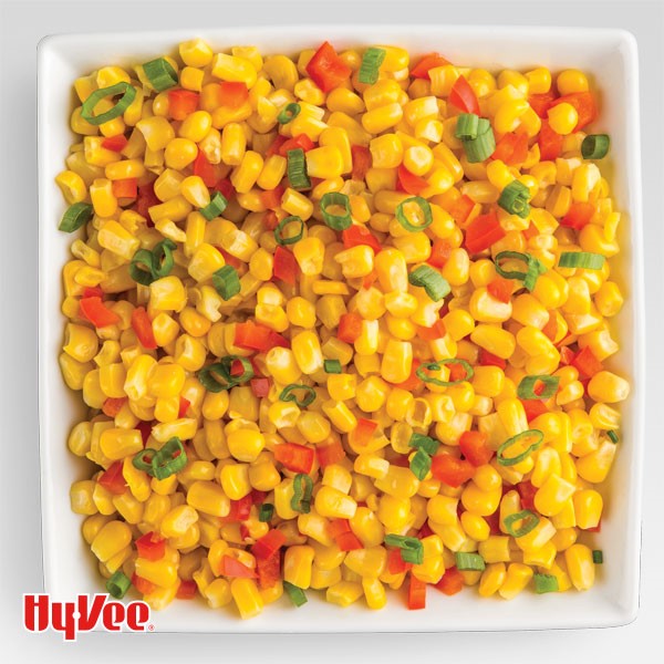 Square white dish filled with corn kernels, red peppers and sliced green onions