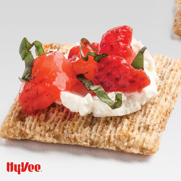 Square cracker topped with cream cheese, strawberries and basil