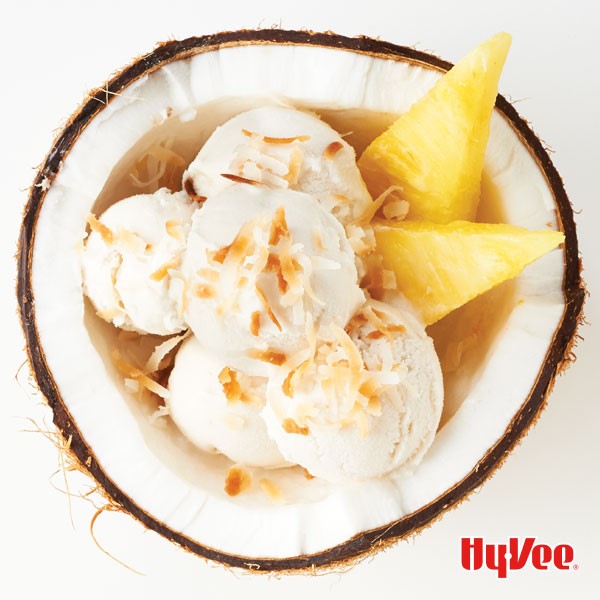 Coconut ice cream topped with toasted coconut with a side of pineapple slices in a coconut bowl