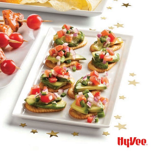 Platter of crackers topped with sliced avocado, pico de gallo and red pepper flakes