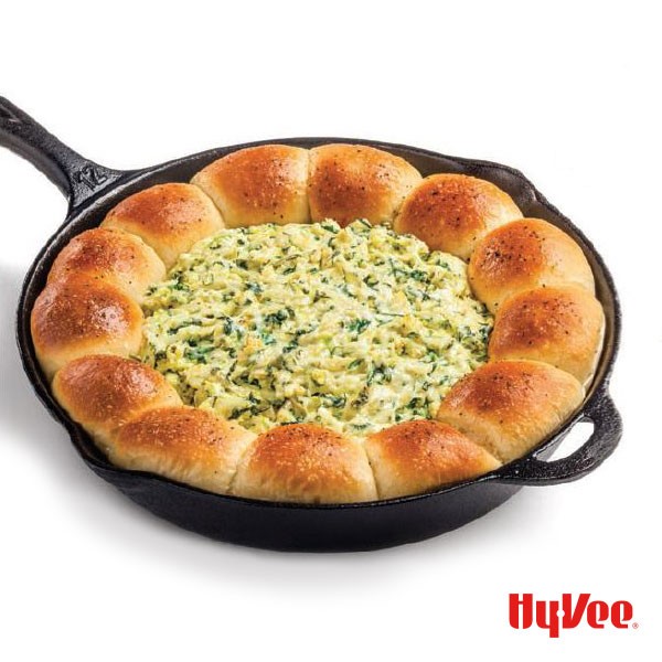 Cast-iron skillet with bread along the inside ring filled with spinach and artichoke dip