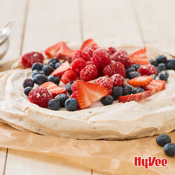 Chocolate chunk pavlova with spiced whipped cream and red berries on parchment paper