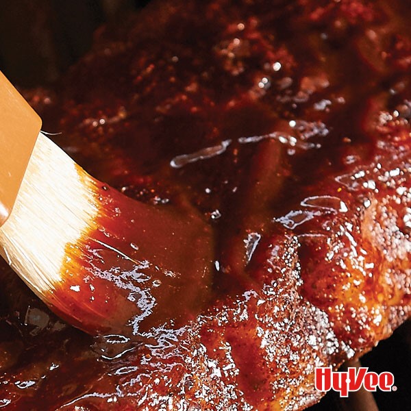 Brush with barbecue sauce glazing ribs on grill