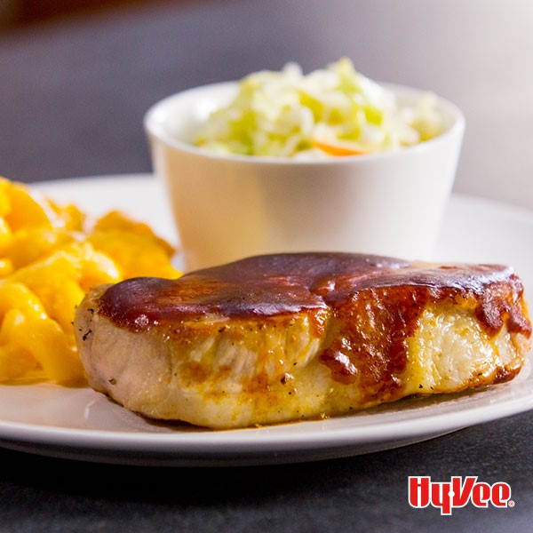 Pork chop topped with barbecue sauce with a side of coleslaw and mac and cheese