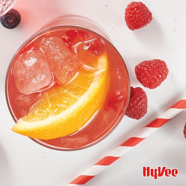 Red raspberry tea drink with ice cubes, orange wedge, and raspberries