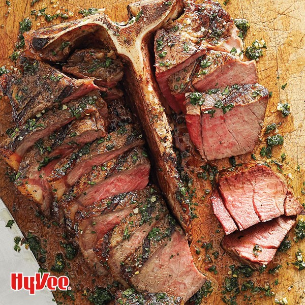 Porterhouse steak covered in herb sauce on a wooden plank